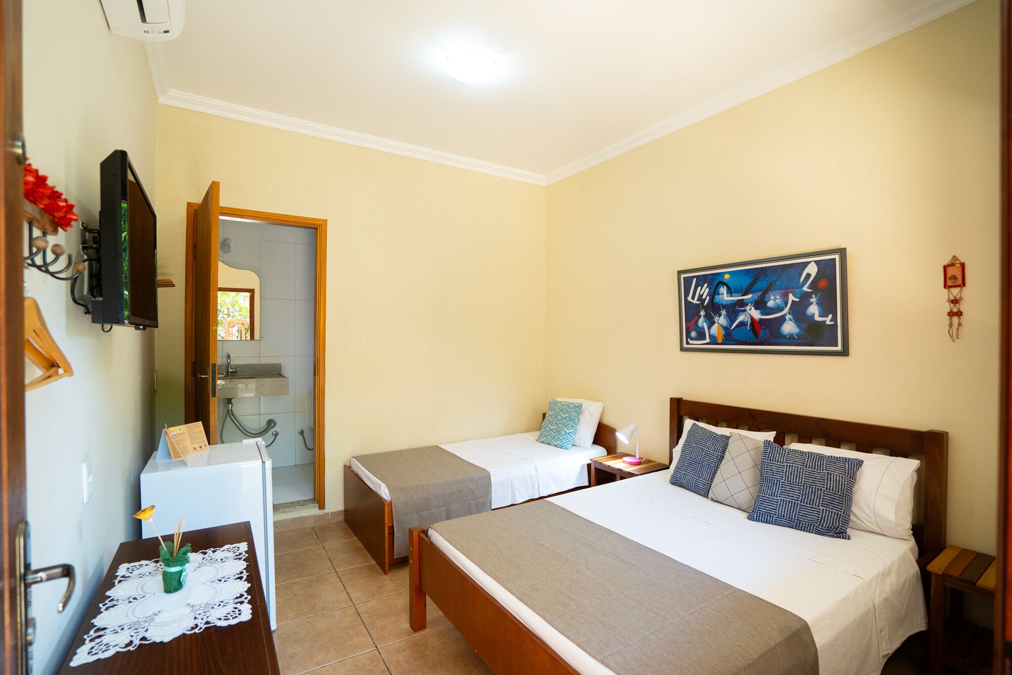 A hotel room with two beds, a desk with a computer, a small table with a decorative item, and a painting on the wall.