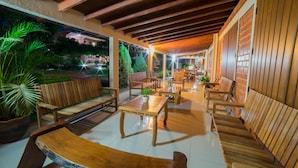 A covered outdoor seating area with wooden furniture and potted plants. - Pousada Galeria Artes (Bonito)