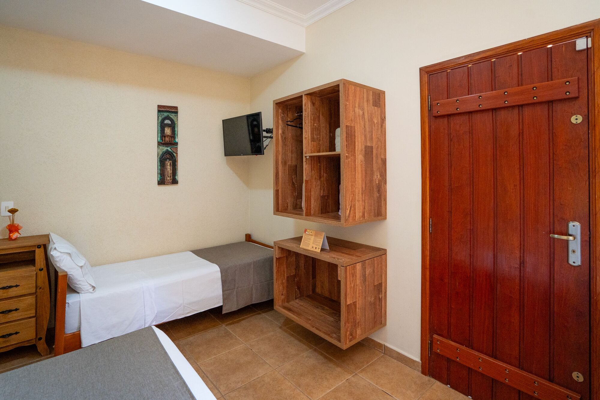 Ein Schlafzimmer mit einem Bett, einem Holzschrank, einem an der Wand montierten Fernseher und einem kleinen Tisch mit einem Schild.