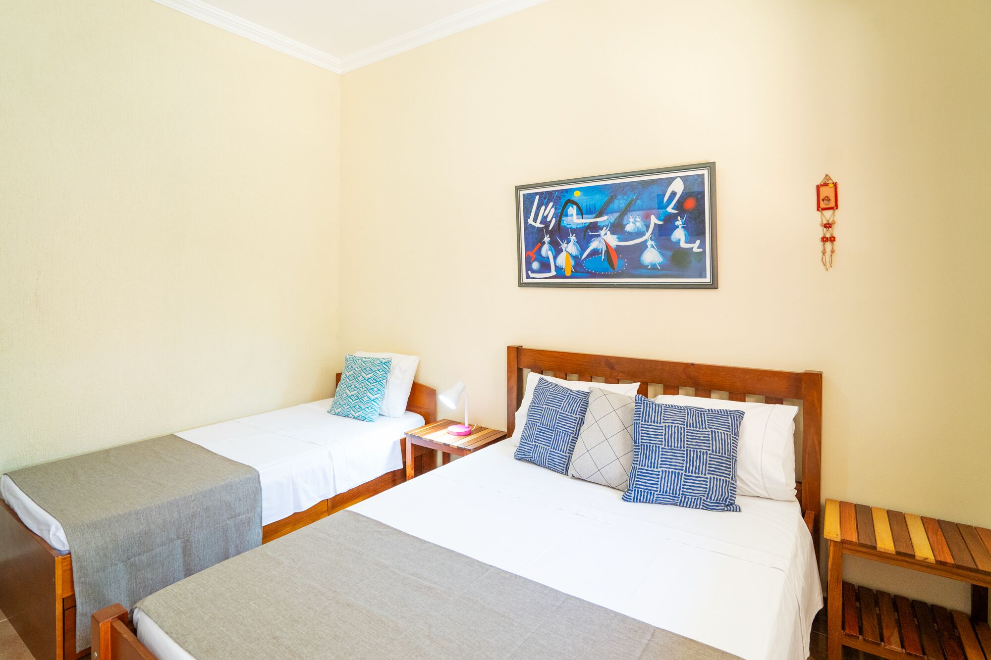 A hotel room with two single beds, a wooden headboard, a nightstand with a lamp, and a wall-mounted painting.