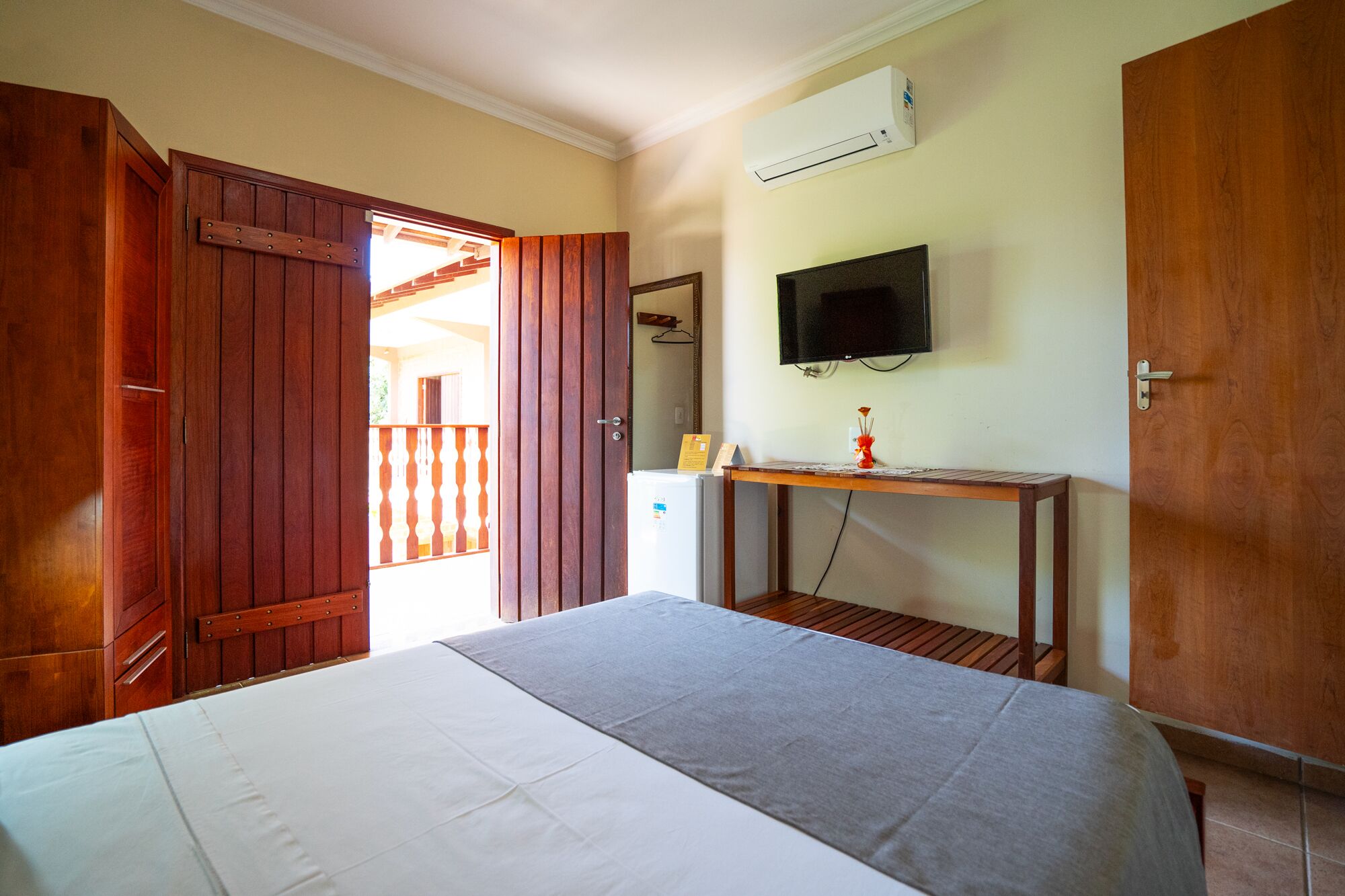 A bedroom with a bed, wooden wardrobe, a desk with a TV, and an air conditioning unit.