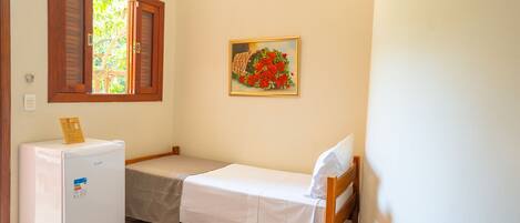 A small, compact room with a single bed, a refrigerator, a window with wooden shutters, and a painting of red roses on the wall.