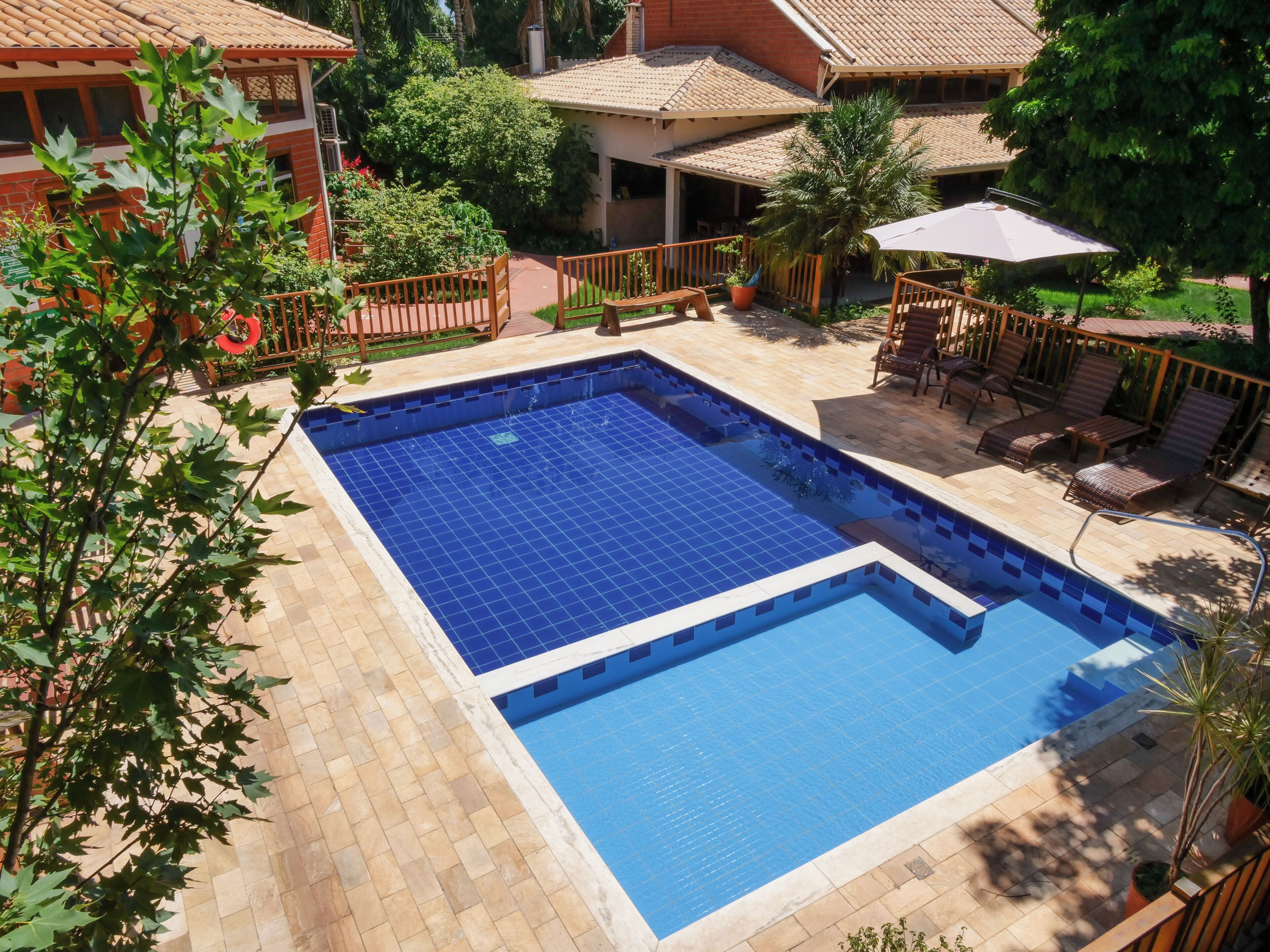 A square swimming pool with tiled edges, surrounded by a patio area with wooden railings and lounge chairs.