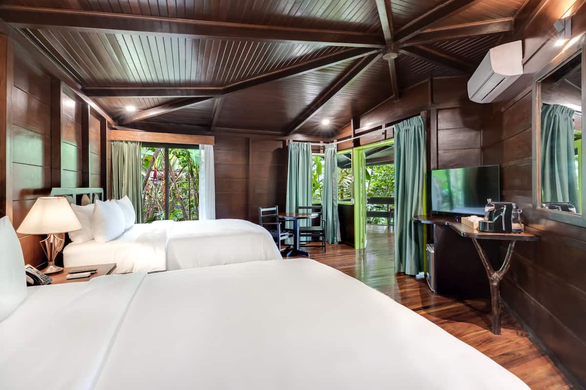 A hotel room with two beds, a desk, a TV, and a balcony with curtains.