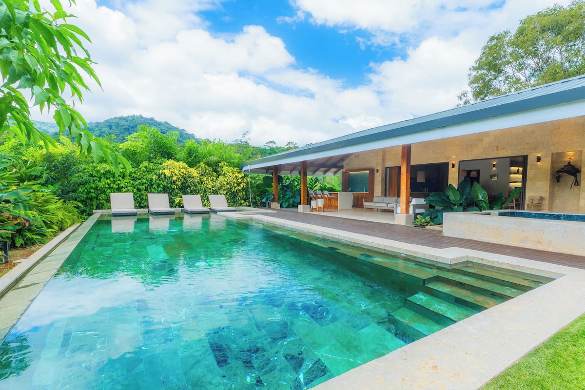 A modern house with a swimming pool, a covered patio, and lush greenery.