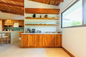 A modern kitchen with wooden cabinetry, a central island, and a large window providing a view of greenery. - Chachagua Rainforest Hotel & Hot Springs (Peñas Blancas)