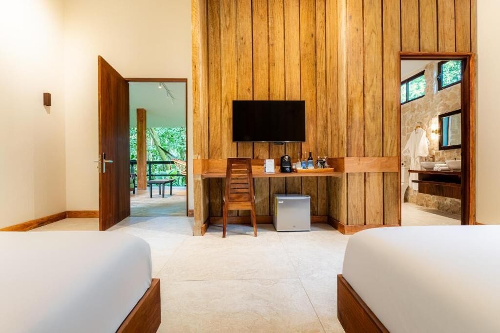 Ein Zimmer mit einem Holztisch, einem Fernseher, einem kleinen Kühlschrank und zwei Betten.