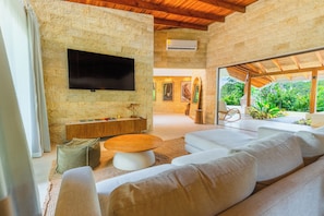 A modern living room with a stone wall, a flat-screen TV, a wooden coffee table, and a large sofa. - Chachagua Rainforest Hotel & Hot Springs (Peñas Blancas)