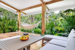 A covered outdoor area with a hammock, a table with fruit, and lush tropical plants.