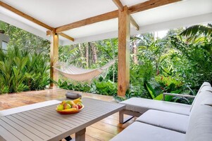 Un espacio al aire libre cubierto con una hamaca, una mesa con fruta y exuberante vegetación tropical.