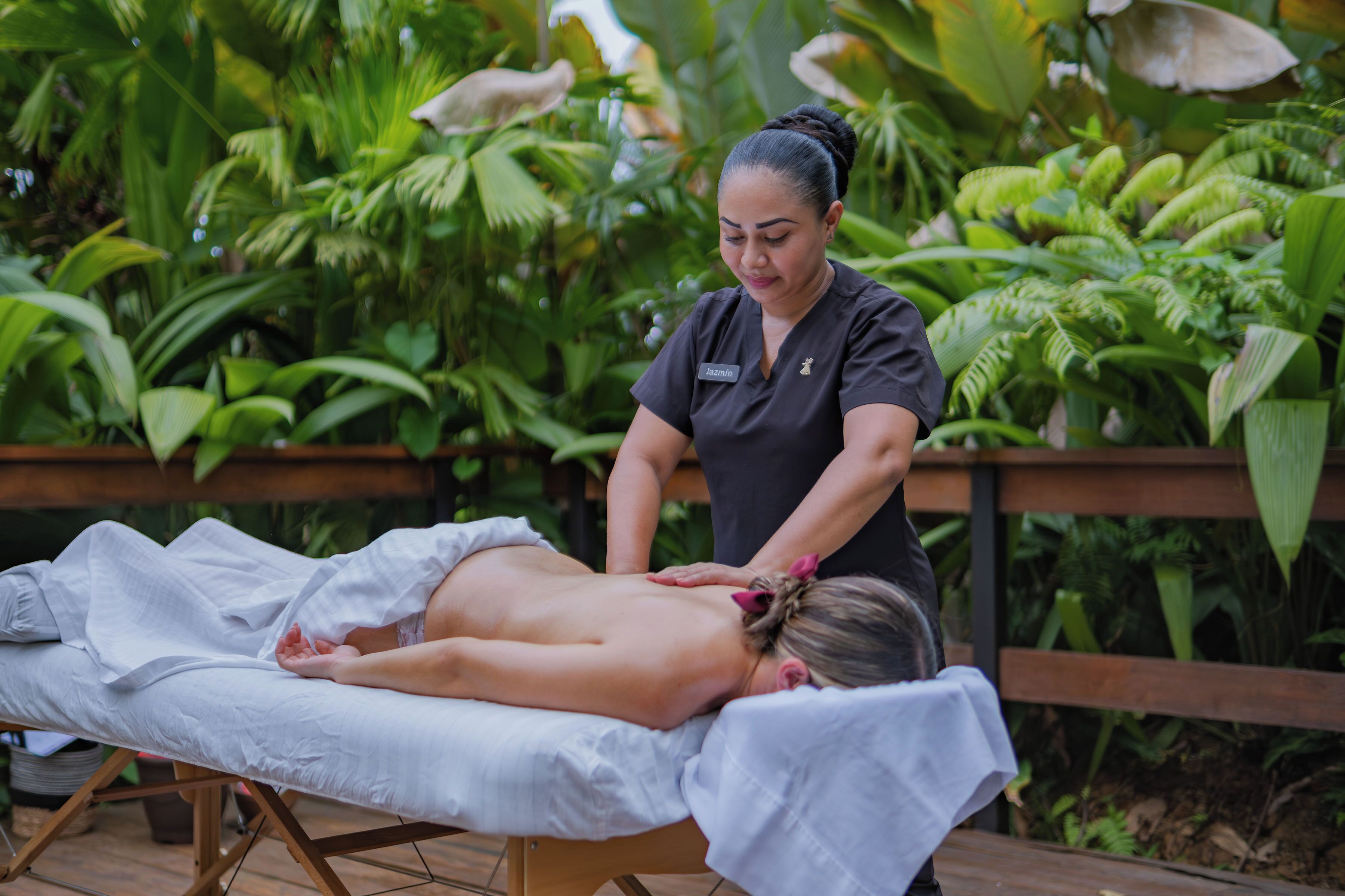 A massage therapy session in an outdoor setting with lush greenery in the background.