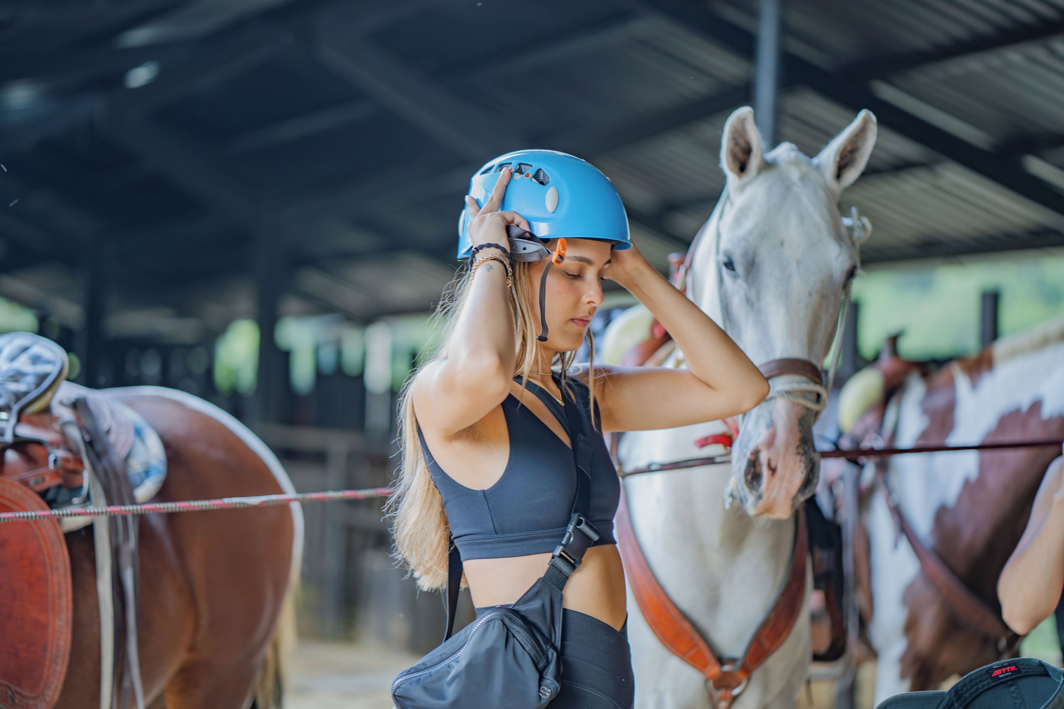 Una persona ajustando un casco en un establo con caballos.