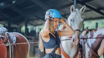 Una persona ajustando un casco en un establo con caballos.