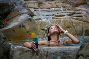 Una persona relajándose en un manantial termal con una bebida.