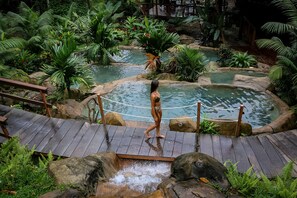 A wooden deck with a rope barrier leading to a pool area surrounded by tropical vegetation.