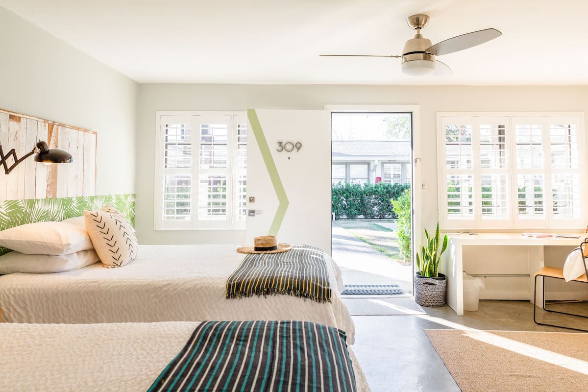 A modern bedroom with two beds, a desk, and a view of the outside.