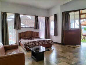 A bedroom with a bed, a coffee table, a sofa, and large windows with curtains. - Nur Alam Hotel Lembang (Lembang)