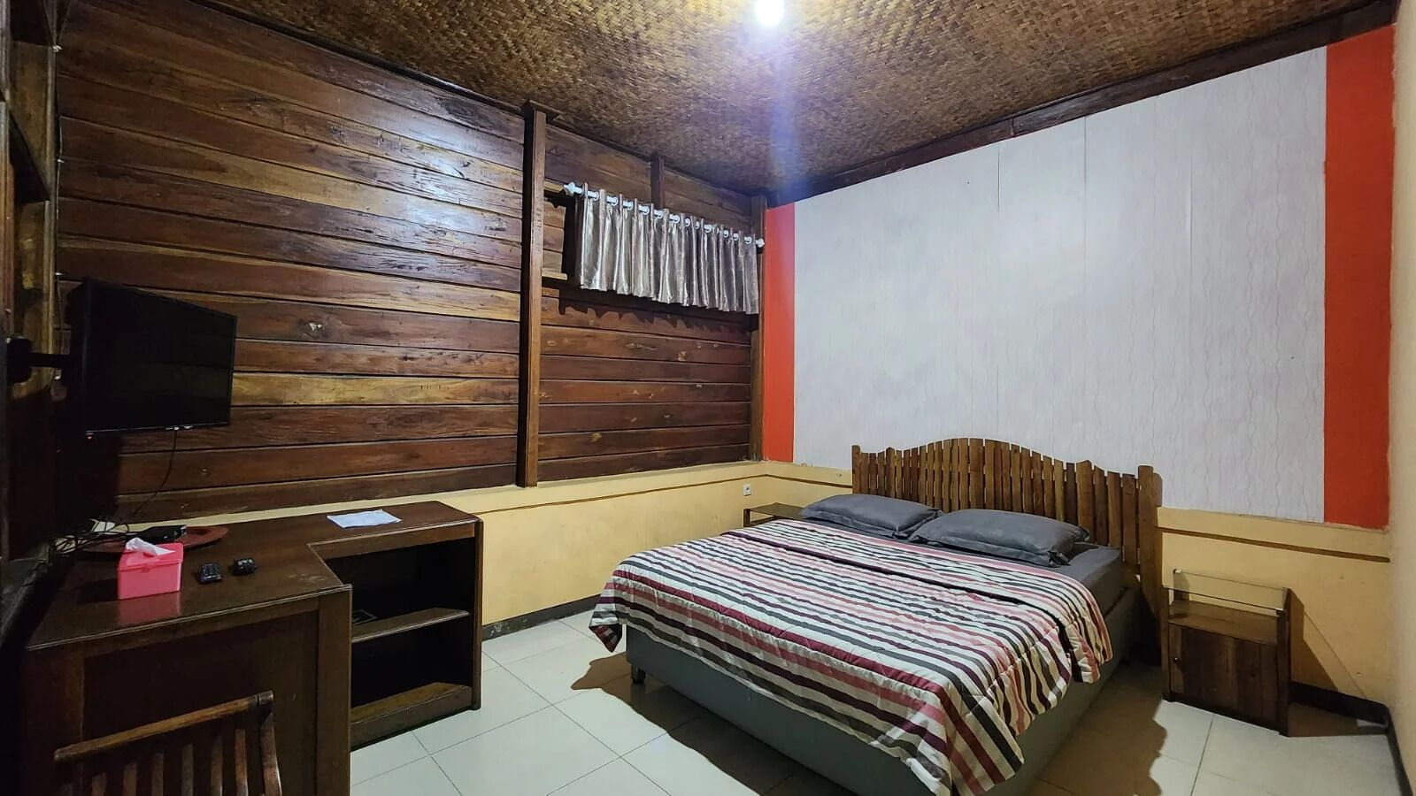 Een kamer met een houten bed, een bureau met een televisie en een gordijn.