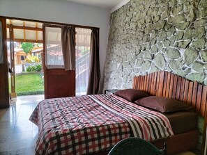 A bedroom with a stone wall, a bed with striped bedding, and a view through an open door. - Nur Alam Hotel Lembang (Lembang)
