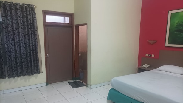 A bedroom with a bed, a door, a window with curtains, a wall-mounted phone, and a small shelf. - Permata Hijau by Zuzu (North Cirebon)