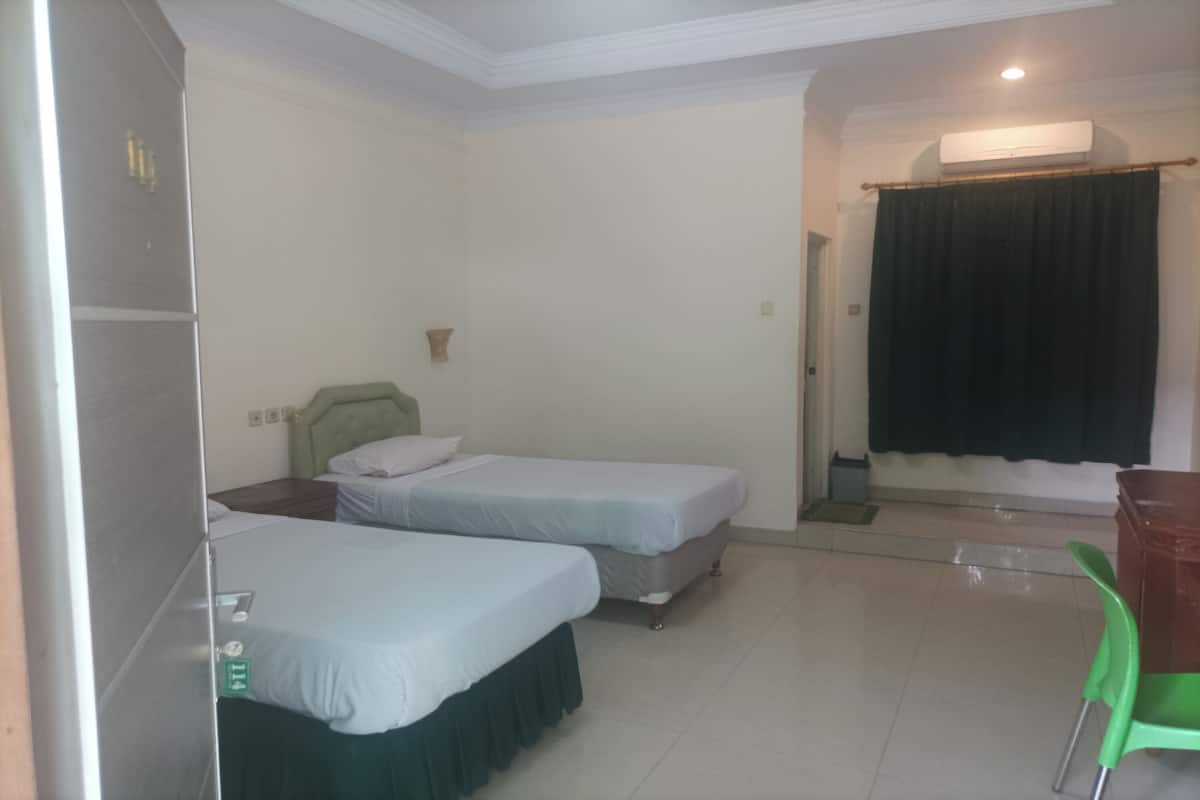 A room with two beds, a desk, a chair, and an air conditioning unit.