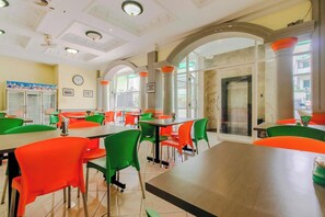 Uma sala de jantar com mesas, cadeiras, janelas amplas e um relógio na parede.