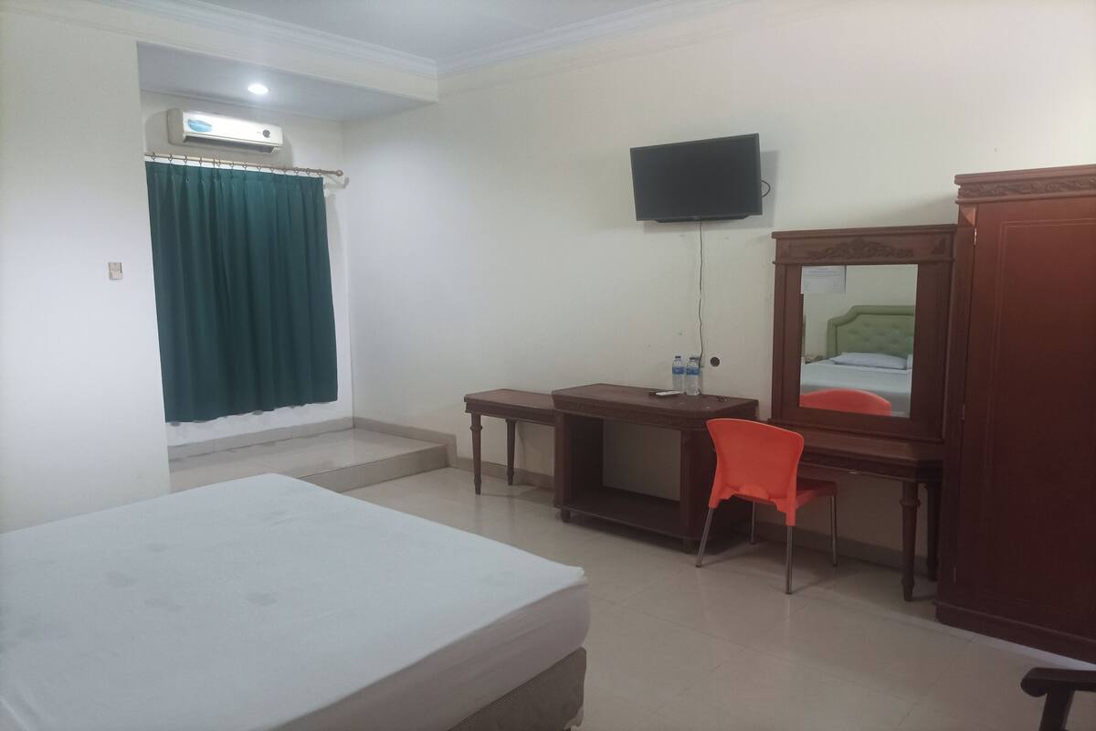 A hotel room with a bed, a desk, a chair, a television, and a wardrobe.