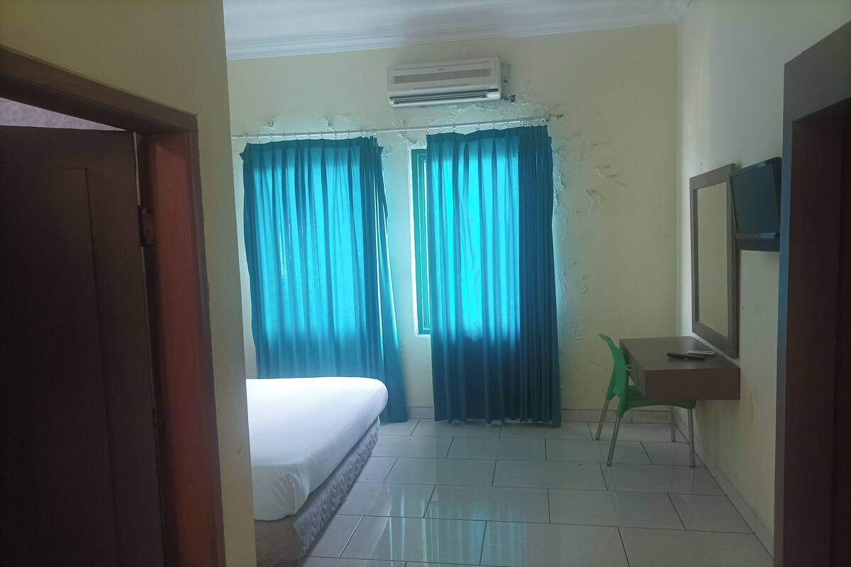 A room with a bed, a desk with a chair, a television, and curtains.