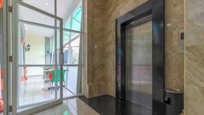A modern elevator, a glass door entrance, and a view of an outdoor seating area. - Permata Hijau by Zuzu (North Cirebon)