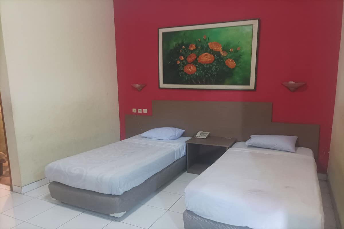 A hotel room with two beds, a painting of flowers on the wall, and a telephone on the nightstand.