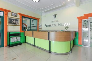 A hotel reception desk with a green and orange color scheme, a framed photo on the wall, and a sign reading 'HOTEL PERNIATA H2-AU'.