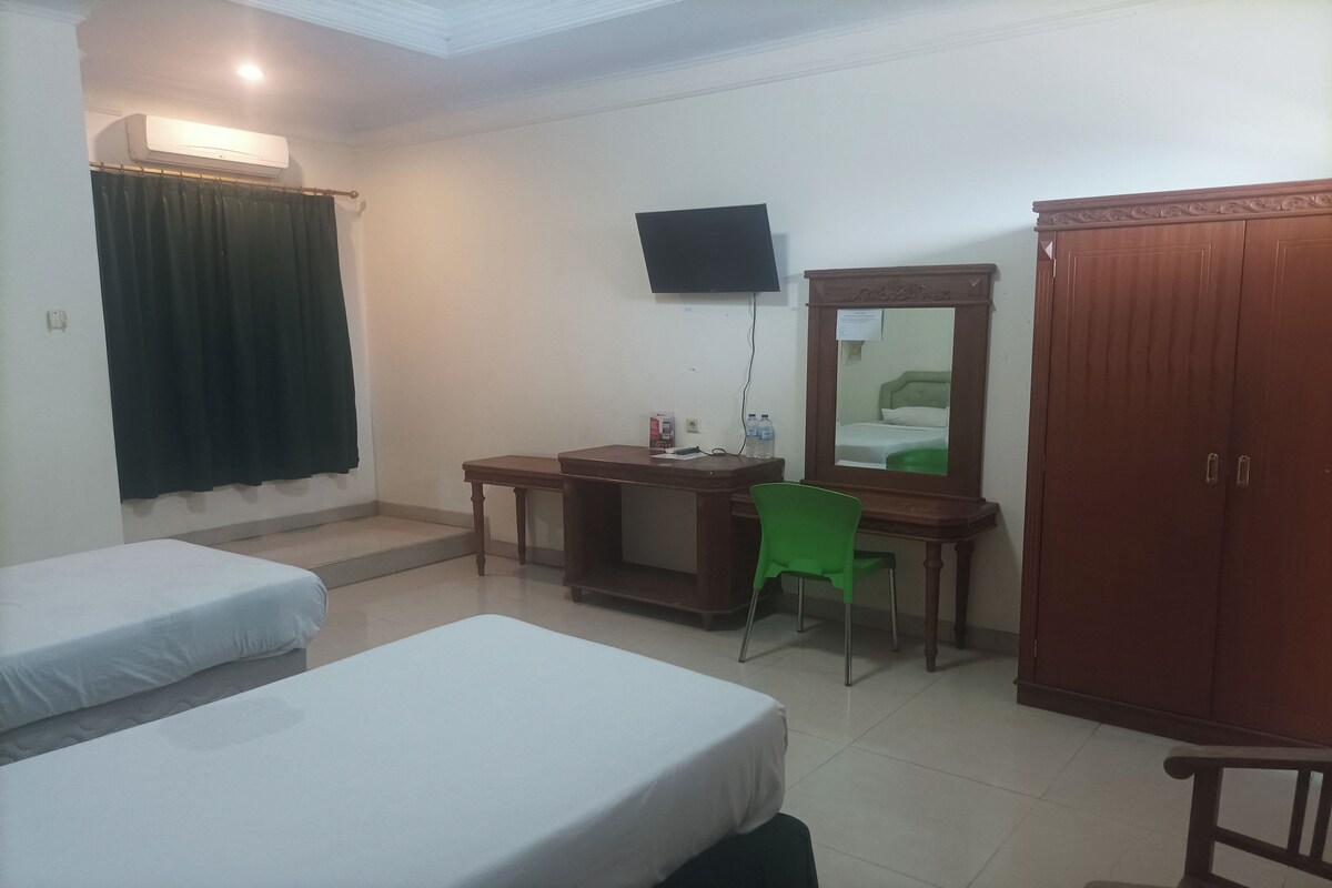 Quarto de hotel com duas camas, uma escrivaninha com cadeira, televisão, guarda-roupa e espelho.