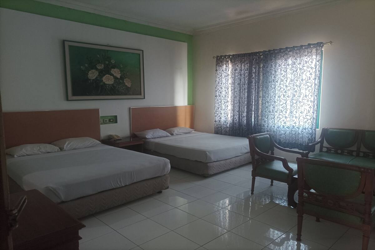 A hotel room with two beds, a desk, a chair, a painting, and a window with curtains.