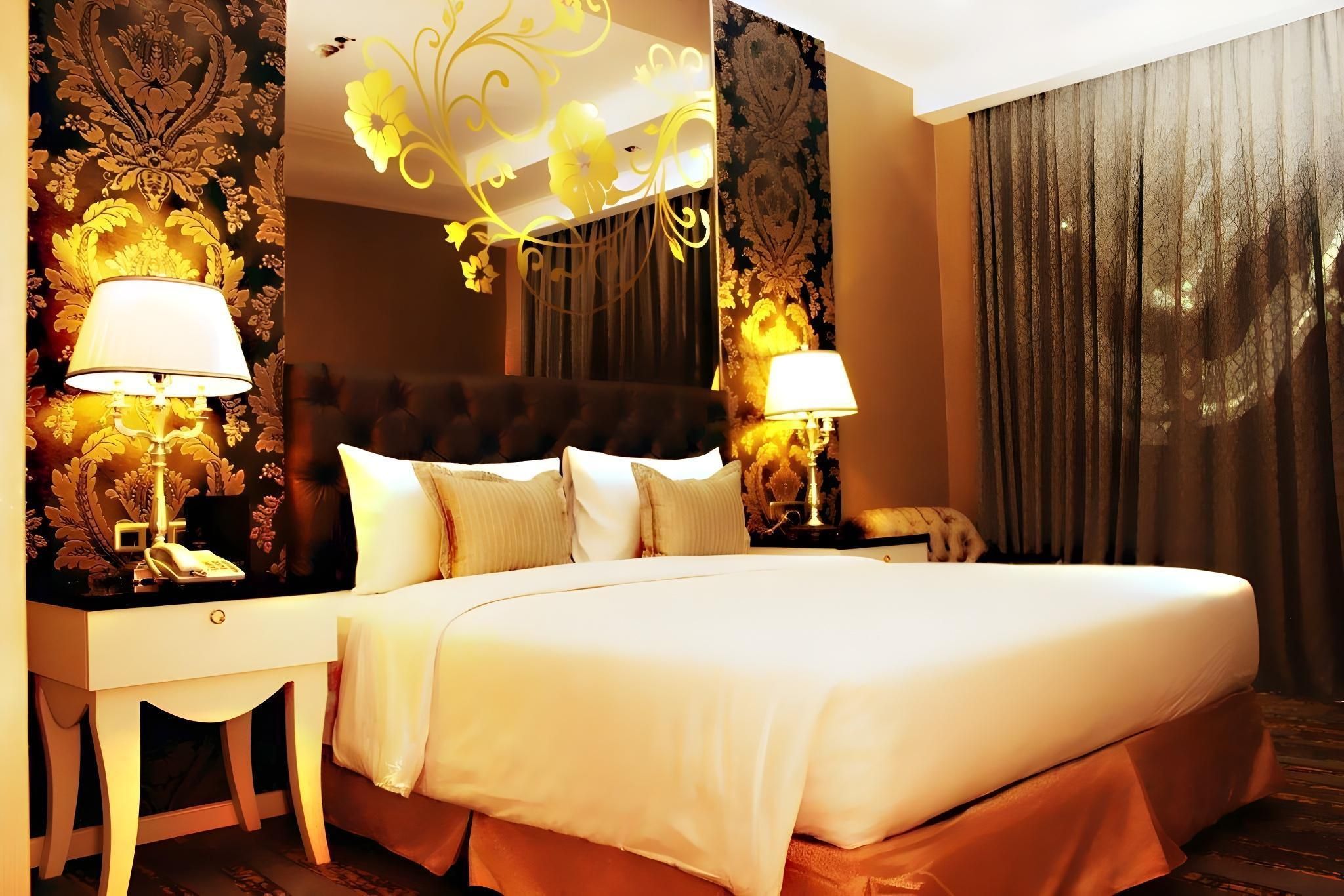 A hotel room with a large bed, two bedside tables with lamps, a decorative headboard, and curtains.