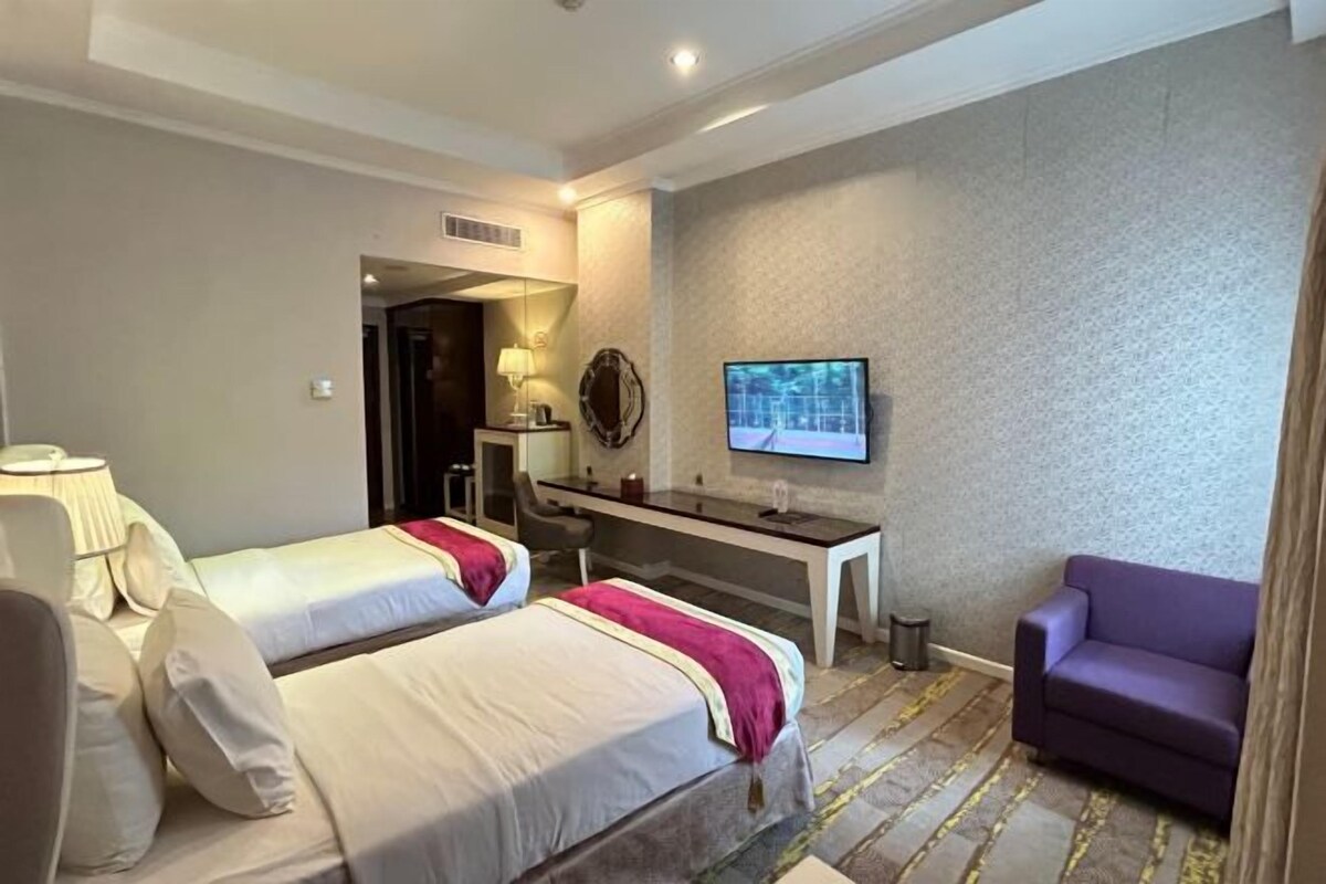 A hotel room with two beds, a desk, a chair, a television, and a purple sofa.