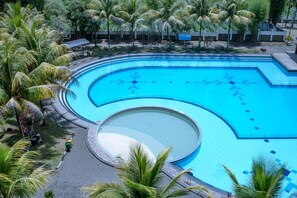 A large, curved swimming pool surrounded by palm trees and a paved walkway. - Sutan Raja Hotel and Convention Cen (Soreang)
