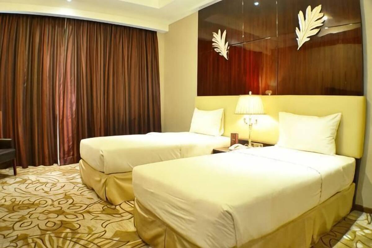 A hotel room with two beds, a desk, a chair, and a large window with curtains.