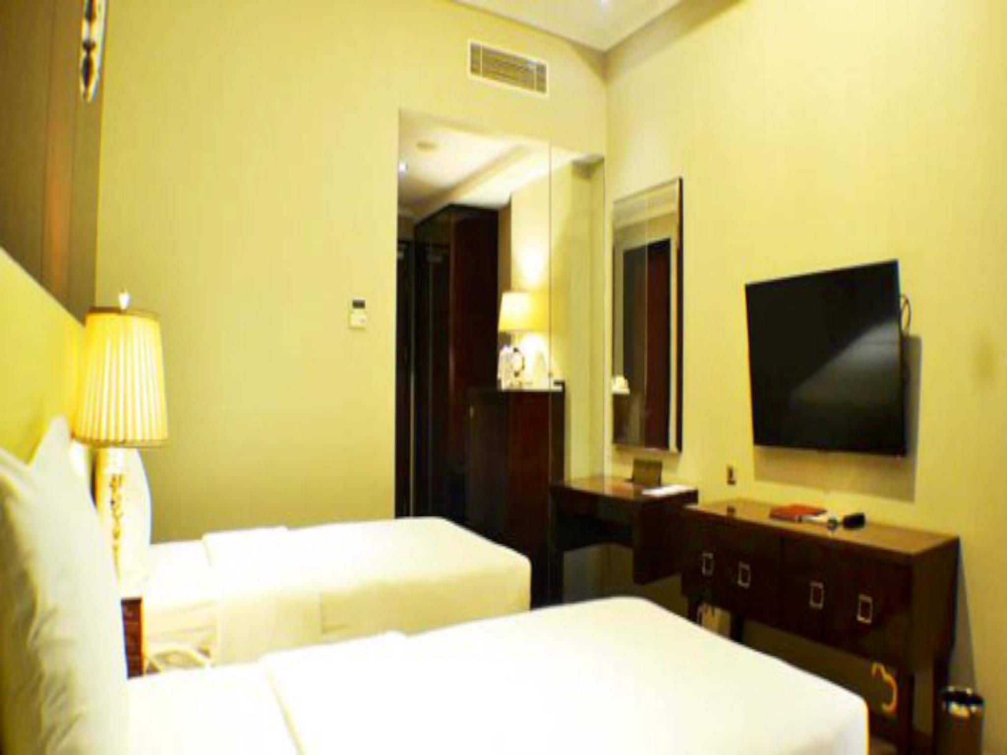 Une chambre d’hôtel avec deux lits, un bureau, une chaise, une télévision et une lampe.