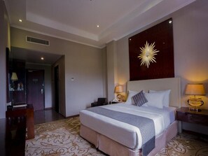 A hotel room with a large bed, two bedside tables with lamps, a decorative wall piece, and a patterned carpet. - Sutan Raja Hotel and Convention Cen (Soreang)