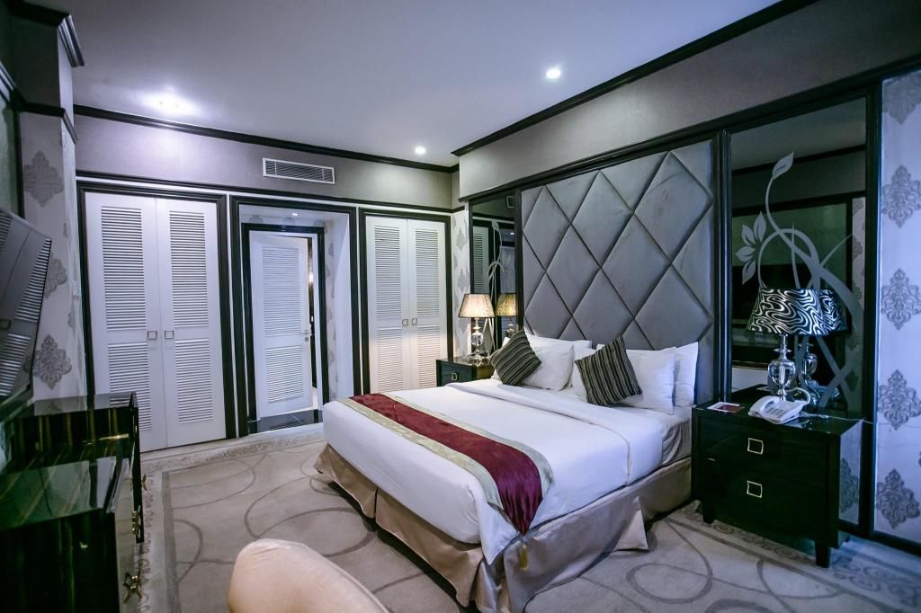 A hotel room with a bed, bedside tables, a desk, and a wardrobe.