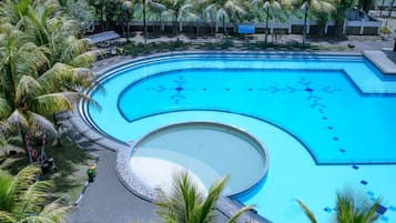 A large, curved swimming pool surrounded by palm trees and a paved walkway.