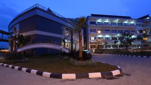A hotel with a curved entrance, a palm tree, and a well-lit building facade. - Sutan Raja Hotel and Convention Cen (Soreang)