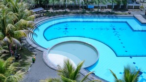 A large, curved swimming pool surrounded by palm trees and a paved walkway. - Sutan Raja Hotel and Convention Cen (Soreang)