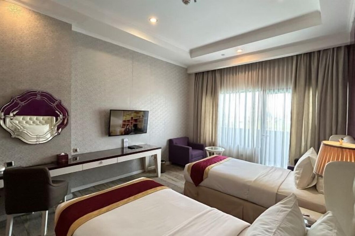 A hotel room with two beds, a desk, a chair, a television, and a window with curtains.
