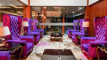 A lobby with purple upholstered armchairs, a central coffee table, and a patterned rug.