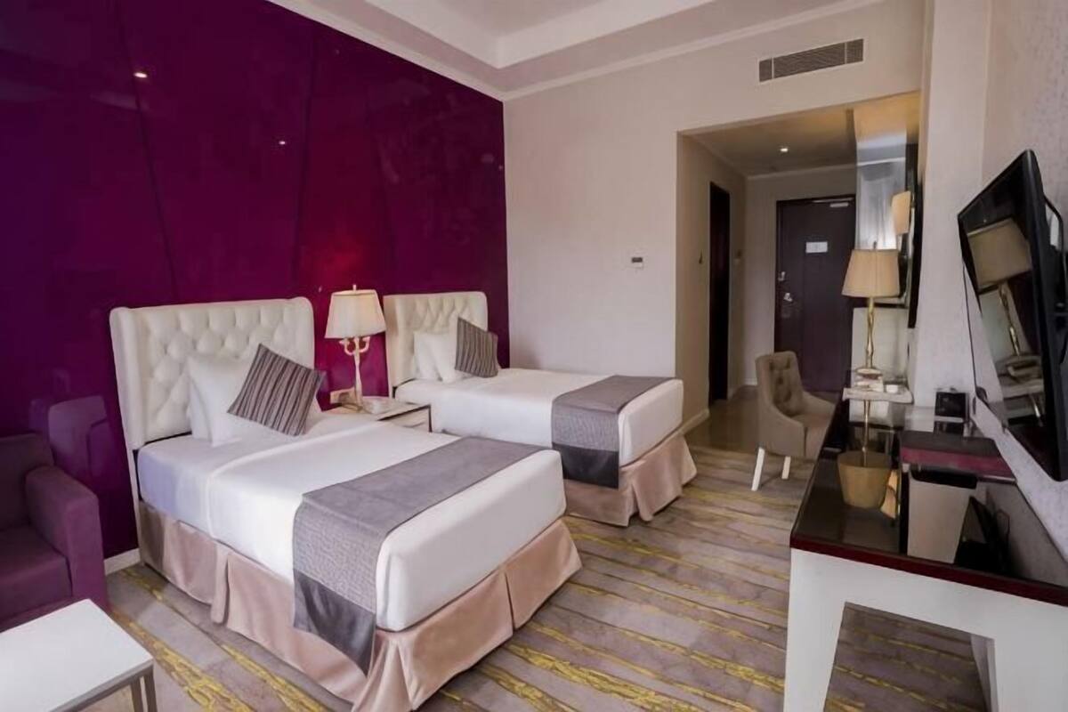A hotel room with two beds, a TV, a desk, and a chair.
