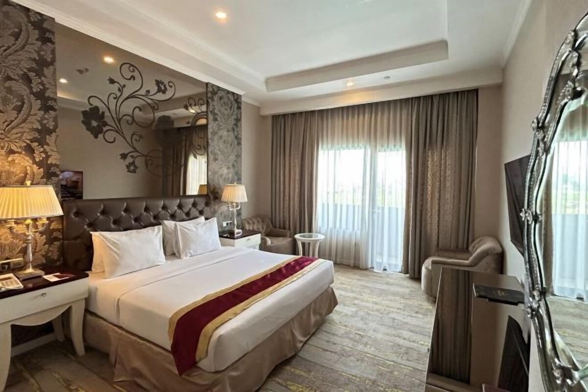 A hotel room with a large bed, a nightstand, a desk, a chair, a mirror, and a window with curtains.