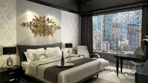 A modern hotel room with a large bed, a desk, and a view of a cityscape through a patterned window. - Sutan Raja Hotel and Convention Cen (Soreang)