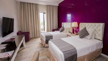 Ein Hotelzimmer mit zwei Betten, einem Fernseher, einem Schreibtisch und einem fensterbepflanzten Fenster.