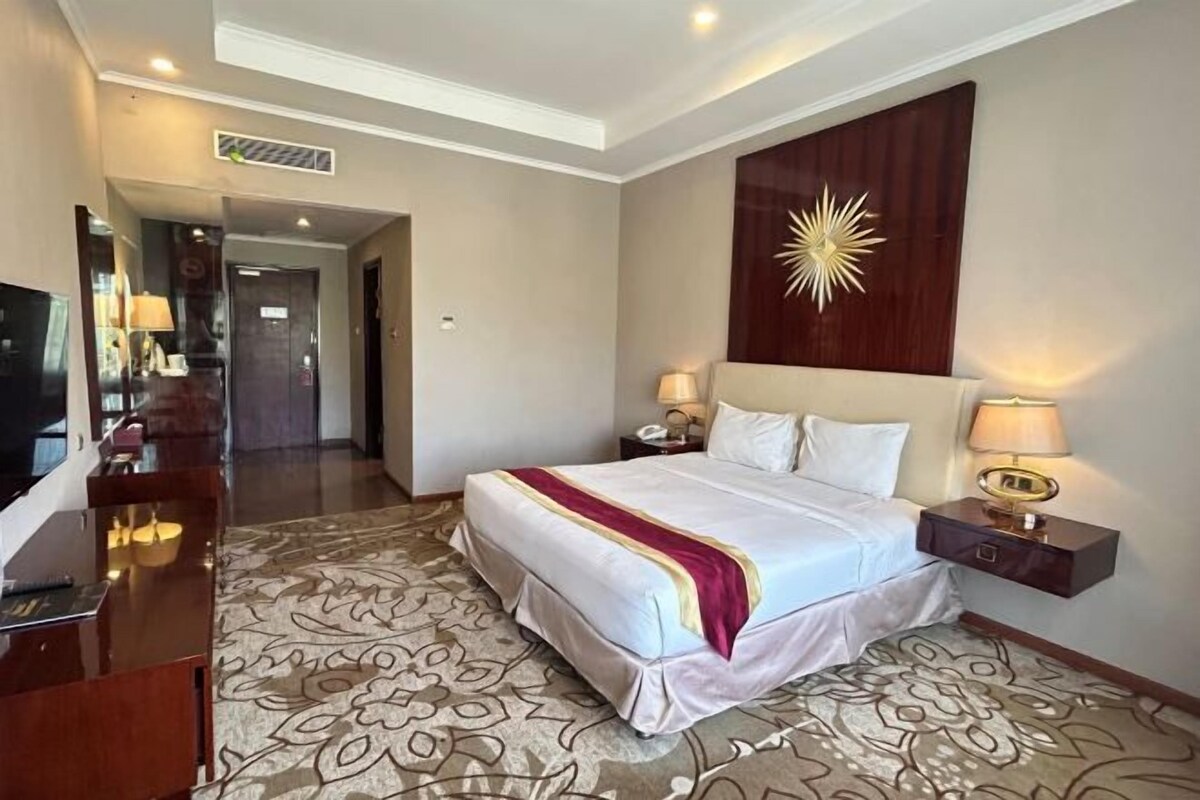 A hotel room with a large bed, bedside tables, a TV, and a decorative wall piece.